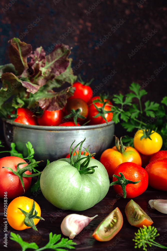 Fresh tomatoes and parsley, dill, garlic on a dark background in a rustic kitchen and wooden utensils still life with copy space