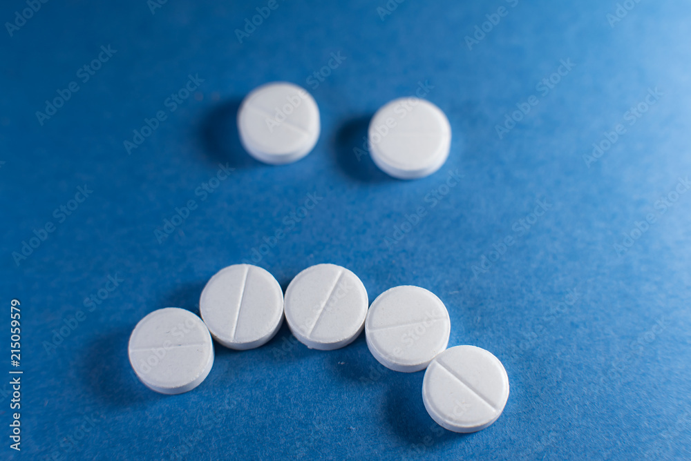 Sad smile made from white pills on blue background