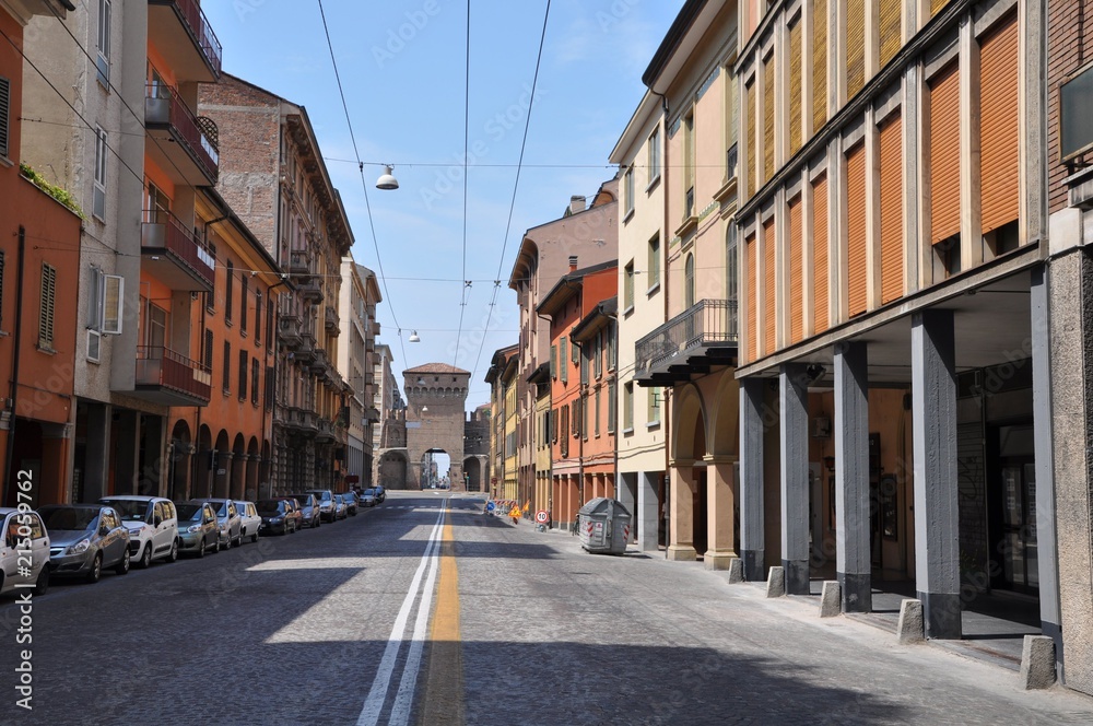Long road and parked cars with orange buildings in Bologna