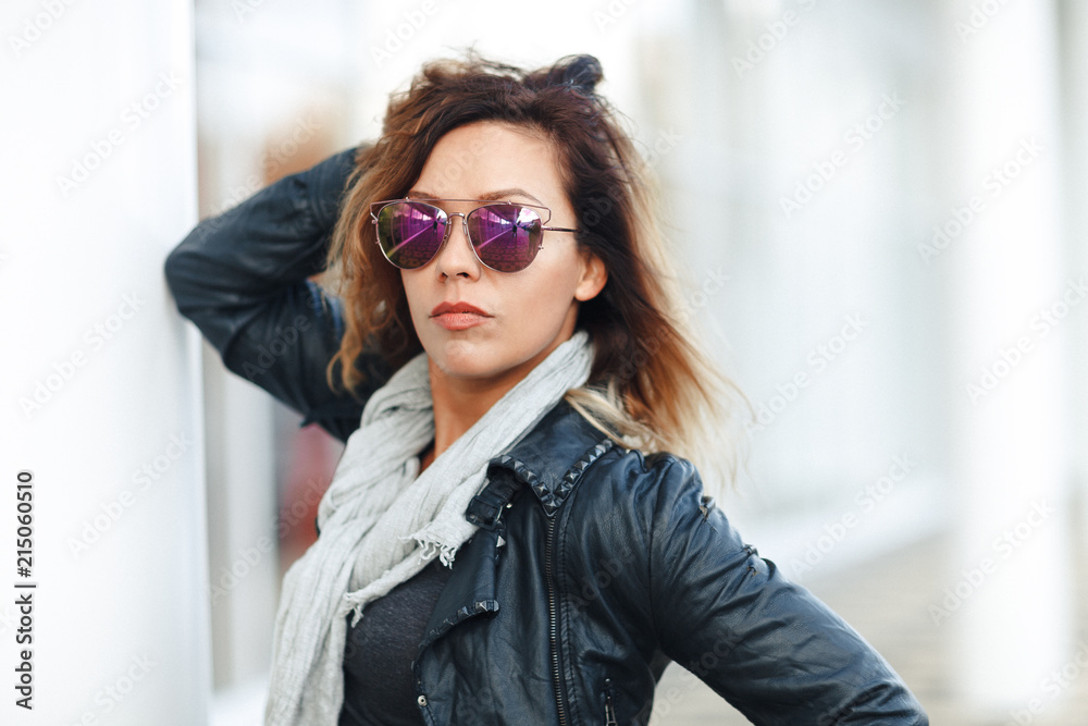 woman in sun glasses a black leather jacket, black jeans posing in front of mirrored windows. Female fashion concept. Outdoor woman in sun glasses a black leather jacket, black jeans posing in front of mirrored windows. Female fashion concept. Outdoor