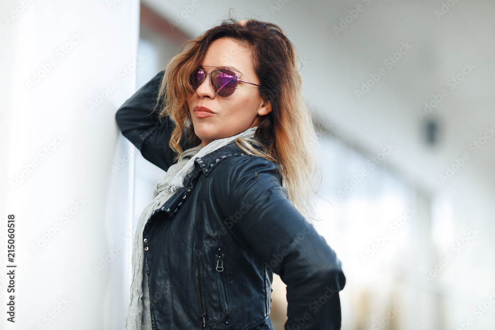 woman in sun glasses a black leather jacket, black jeans posing in front of mirrored windows. Female fashion concept. Outdoor woman in sun glasses a black leather jacket, black jeans posing in front of mirrored windows. Female fashion concept. Outdoor