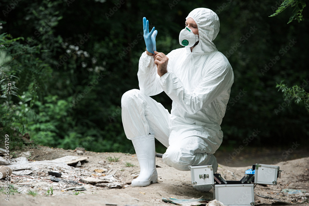male scientist in protective mask and suit putting on latex glove in forest male scientist in protective mask and suit putting on latex glove in forest