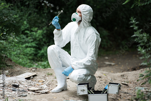 focused male scientist in protective suit and mask examining stone while holding by tweezers in forest © LIGHTFIELD STUDIOS