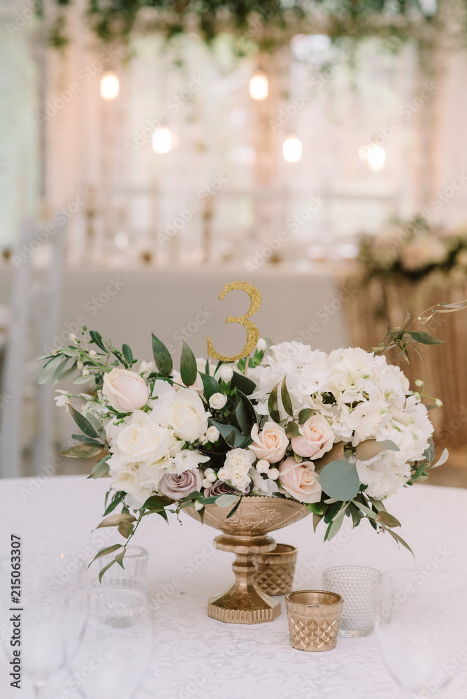 Decoration of a banquet table at a wedding with flowers in a gold vase.