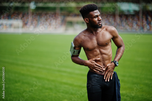 African american male athlete sexy sport bare torso man with running sports arm case for mobile phone, posed at green grass of football stadium.