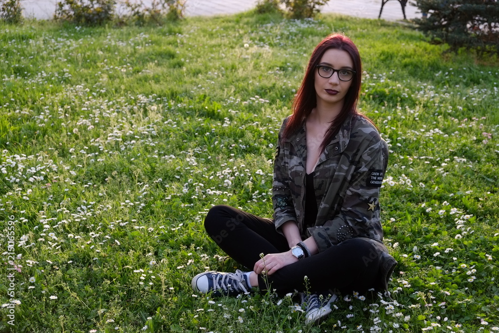 Military style girl sitting in a park on a grass full with flowers Military style girl sitting in a park on a grass full with flowers