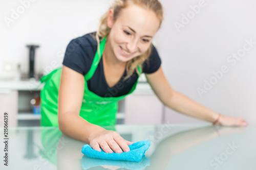 cleaning service. a young woman in an apron wipes dust with a rag