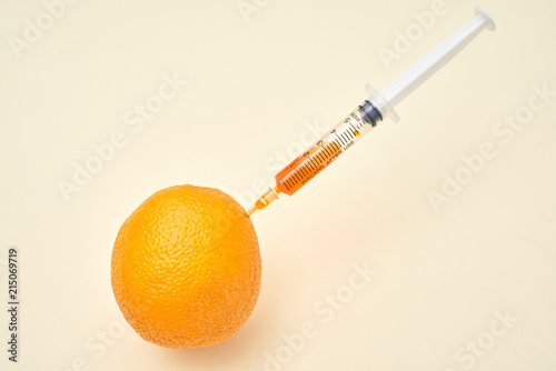 Bright ripe orange fruit with syringe extracting liquid and showing concept of cellulite treatment on white background