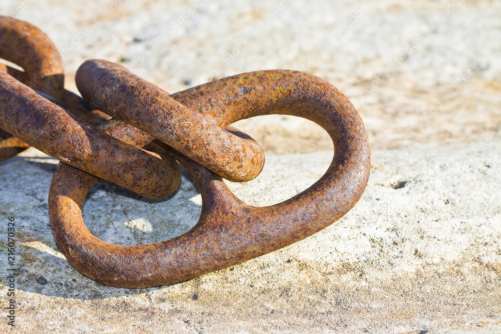 Detail of an old rusty metal chain anchored to a concrete block Detail of an old rusty metal chain anchored to a concrete block