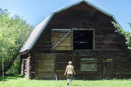 rear view of a middle aged Caucasian woman walking toward a large antique barn with an open hayloft on a sunny summer day