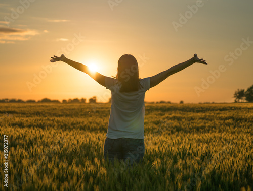 A sillhouette of a happy woman standing in a wheat field in summer.