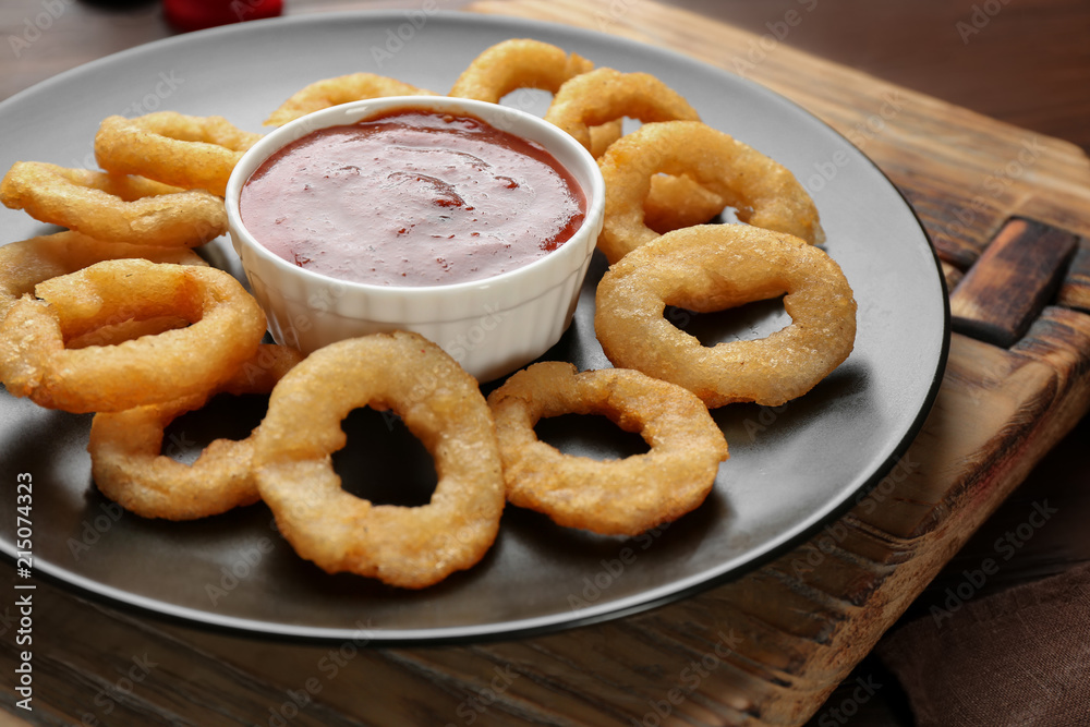 Plate with fried onion rings and sauce on table