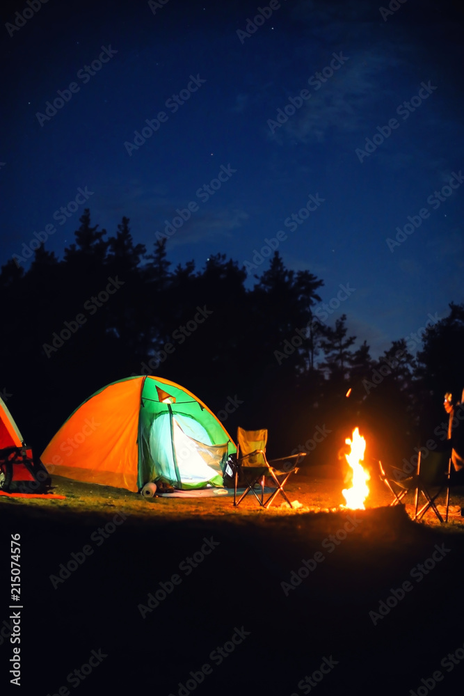 Glowing camping tent near bonfire in wilderness at night Glowing camping tent near bonfire in wilderness at night