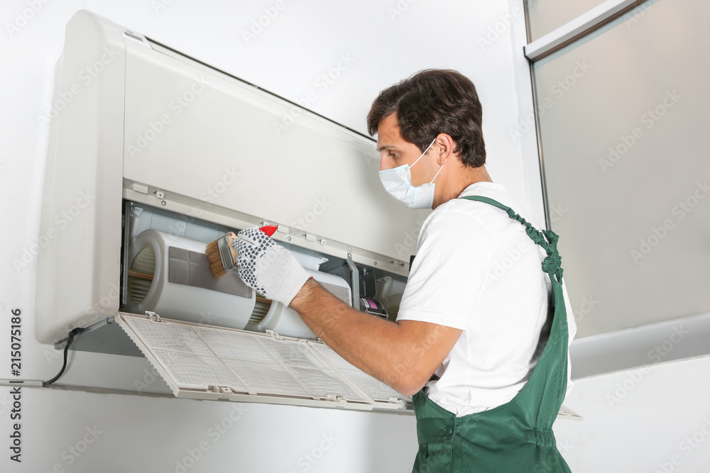 Obraz premium Young male technician cleaning air conditioner indoors