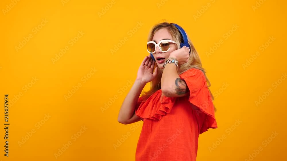 Gorgeous happy woman wears sunglasses and headphones dances and listens to music on yellow orange background. Sexy woman in summer dress. Copyspace available Gorgeous happy woman wears sunglasses and headphones dances and listens to music on yellow orange background. Sexy woman in summer dress. Copyspace available