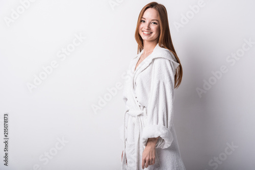  Beautiful red-haired girl in a white bathrobe on a light background