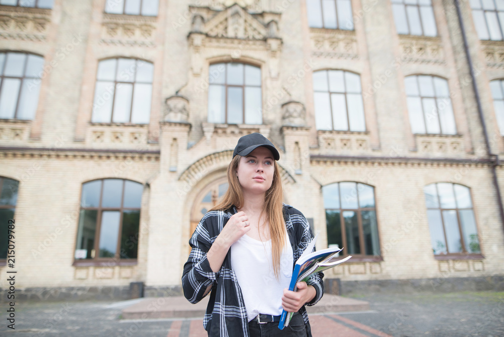 Сute student girl walking on campus with books and books in his hands. Portrait of an attractive student in casual clothing.