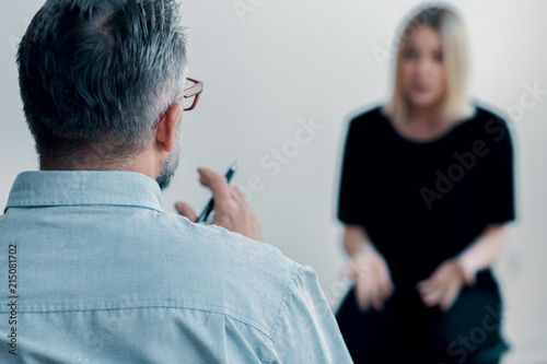 Close-up of a therapist holding a pen talking to his blurred female patient photo