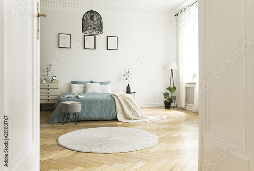 White round rug in spacious bedroom interior with green bed under lamp and posters. Real photo