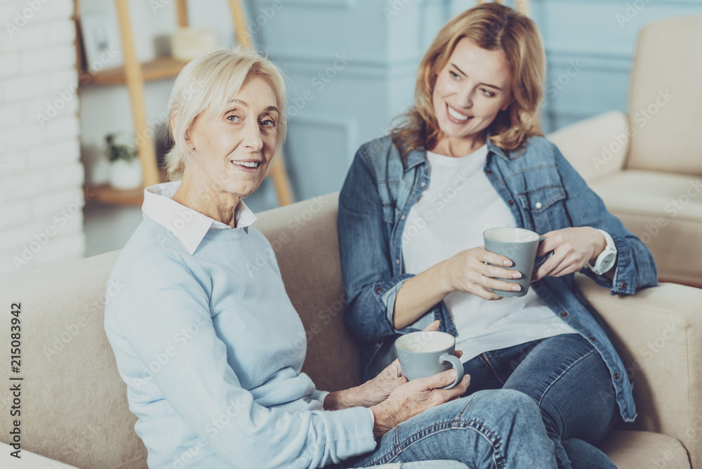 Two generations. Pleased girl holding cup in both hands while having friendly talk Two generations. Pleased girl holding cup in both hands while having friendly talk