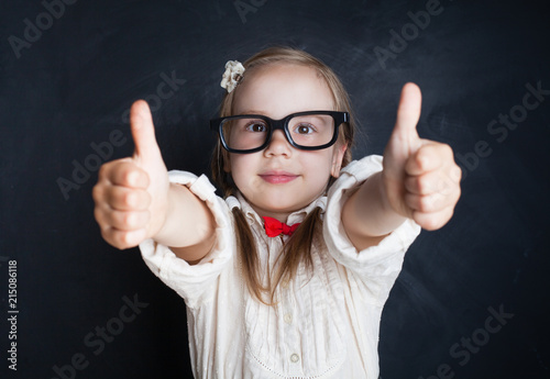 Smart Child Little Girl with Thumb Up Having Fun in Classroom on Chalk Board Background. Back to school  Creativity and Education Concept