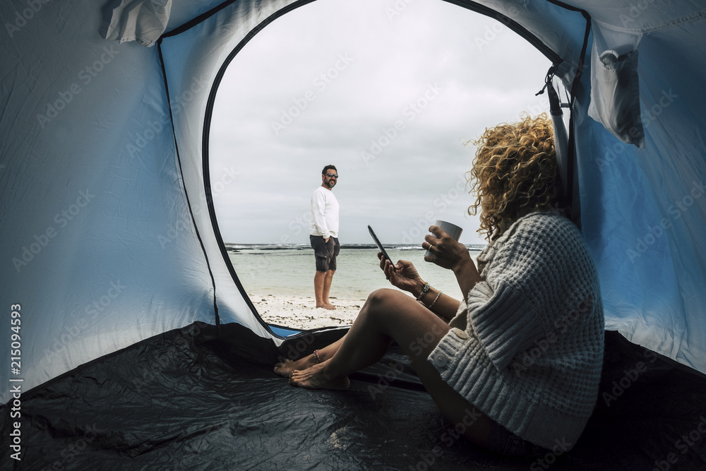 couple of caucasian traveler people camping on the beach near the ocean waves, paradise vacation alternative lifestyle with tiny house and enjoying the outdoor leisure activity. modern technology.