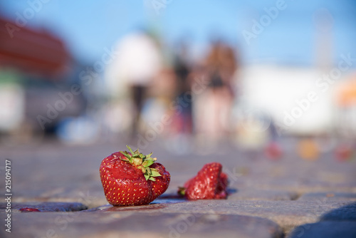 Two dropped and slightly damaged strawberries on the cobblestone ground at the Market square in center of Helsinki on a hot July evening.