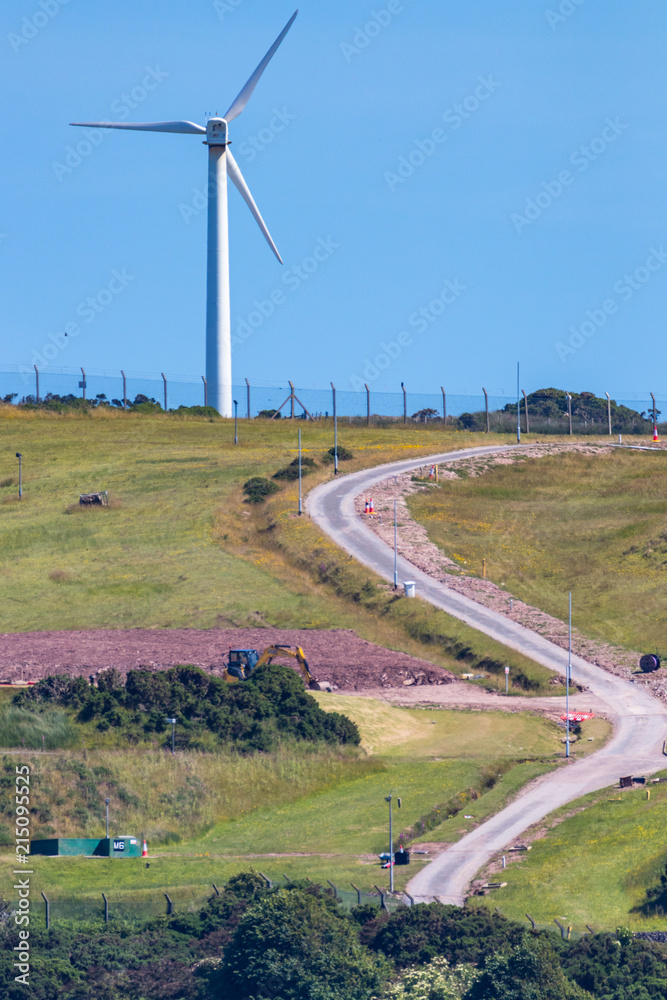 Vertical photo of a single wind turbine on a green hill with a winding road and a blue sky. Vertical photo of a single wind turbine on a green hill with a winding road and a blue sky.