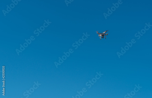 Modern Drone with camera flying on blue sky background.