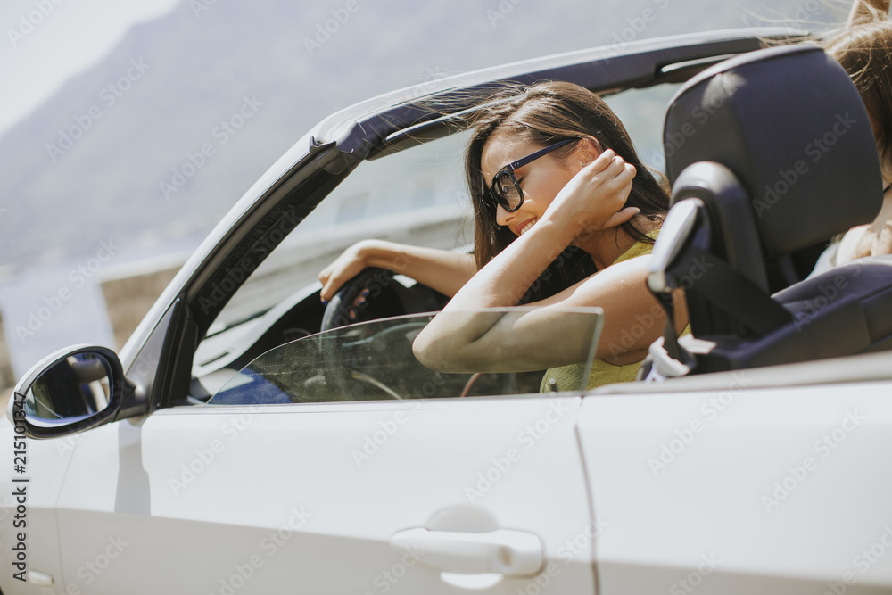 Naklejka premium Young woman with sunglasses driving her convertible top automobile on bright sunny day