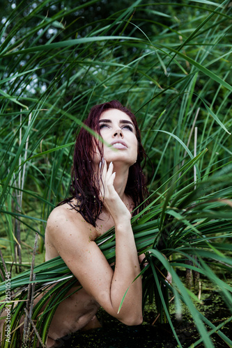 young naked woman in a thicket of reeds in a swamp, looking up
