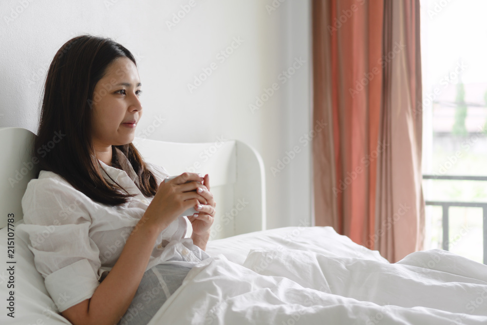 Young asian woman drinking morning coffee in bed. Young asian woman drinking morning coffee in bed.