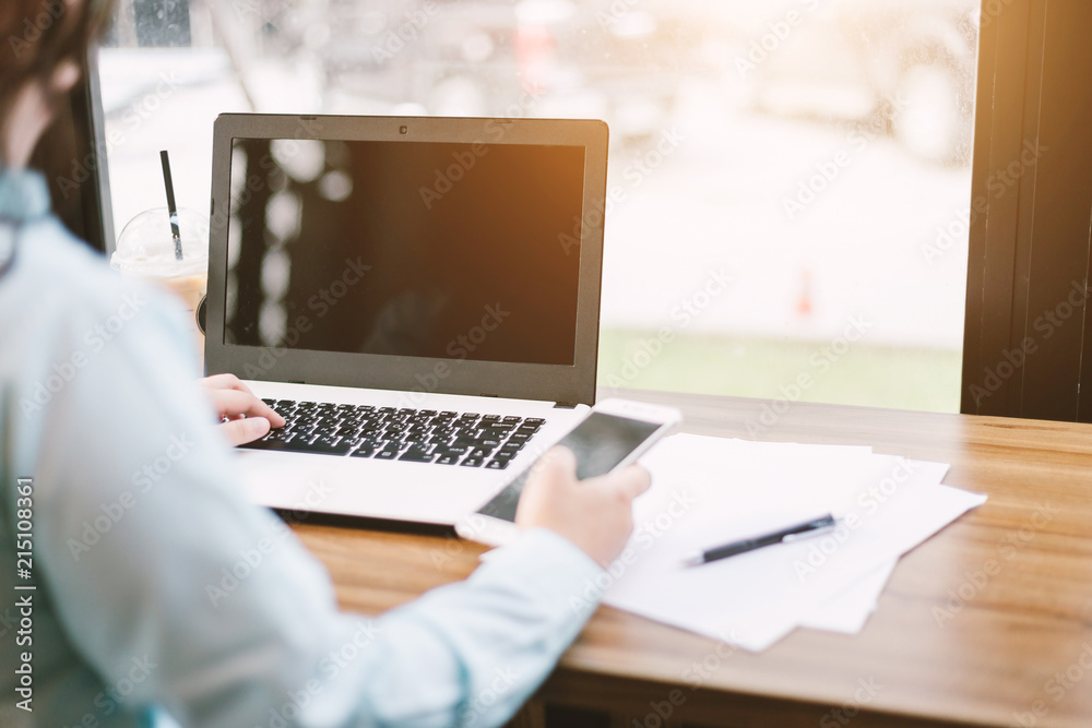 Fototapeta premium Close-up of business female working with Mockup image of laptop with blank black screen make a note in coffee shop like the background.