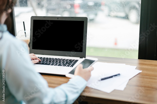 Close-up of business female working with Mockup image of laptop with blank black screen make a note in coffee shop like the background. © Thinapob