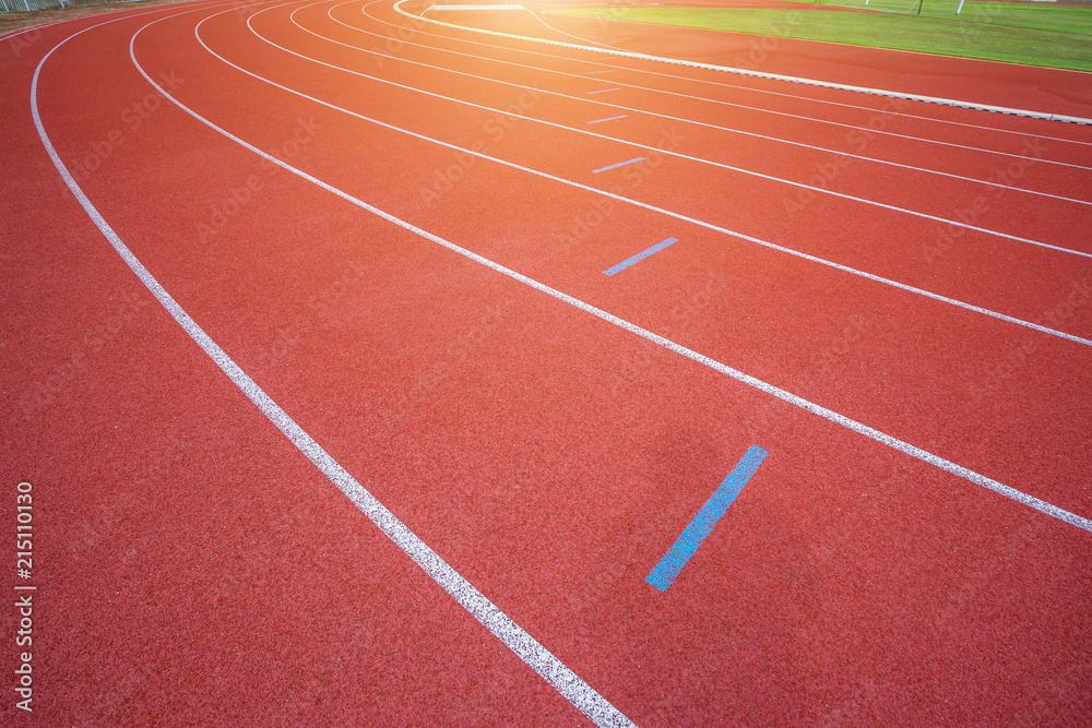 Fototapeta premium White lines of stadium and texture of running racetrack red rubber racetracks in outdoor stadium are 8 track and green grass field,empty athletics stadium with track.