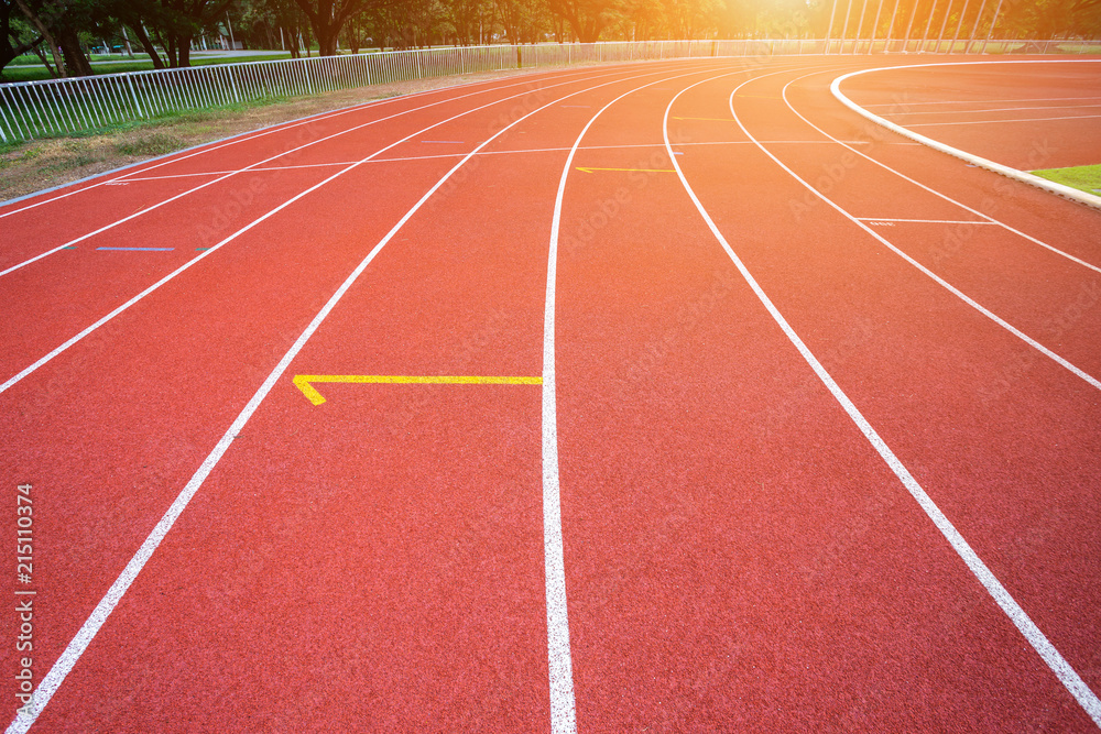 Fototapeta premium White lines of stadium and texture of running racetrack red rubber racetracks in outdoor stadium are 8 track and green grass field,empty athletics stadium with track.