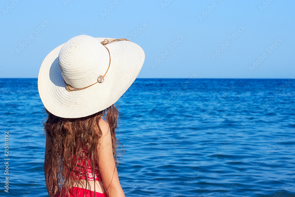 Cute teenager girl wearing at a big hat and swimwear looking at the sea. Place for text