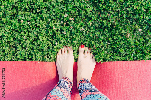 Women's legs with red nails in colored leggings are on a yoga Mat on the grass, on a Sunny summer day. The view from the top, space for text