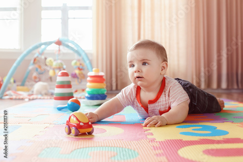 Portrait of cute adorable blond Caucasian smiling child boy with blue eyes crawling on floor in kids children room. Little baby playing with toys on playmat at home. Early education development