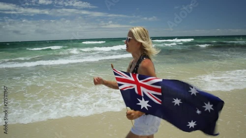close up of woman running on white beach waving Australian Flag. Blonde lifestyle tourist enjoying in Mettams Pool, North Beach near Perth in Western Australia. Blue sky, summer holiday. Copy space. photo