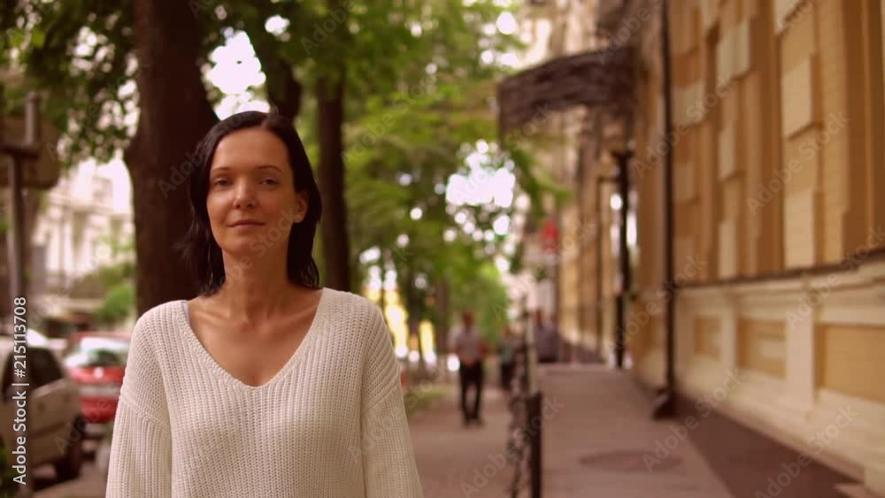 cheerful lady walks along the sideway. female wears white casual pullover. cheerful lady walks along the sideway. female wears white casual pullover.