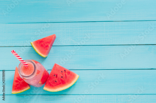 Top view of watermelon slices and juice in a glass bottle on a turquoise background (copy space)