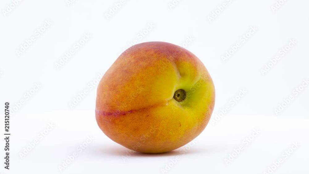 One peach fruit is rotating on the turntable isolated on the white background. Close up. One peach fruit is rotating on the turntable isolated on the white background. Close up.