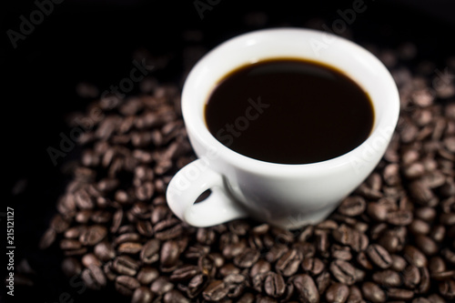 Black coffee in white cup with coffee beans on dark surface. Close up.