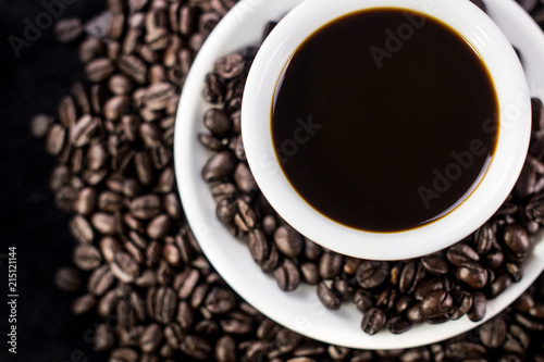 Dark coffee in white plate with coffee beans on black background.