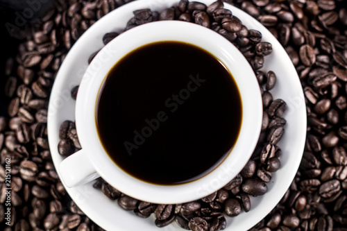 Dark coffee in white plate with coffee beans on black background.