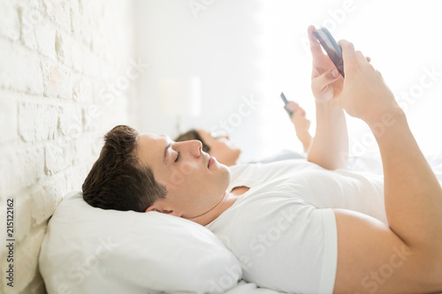 Man Messaging On Smartphone While Lying By Woman In Bed