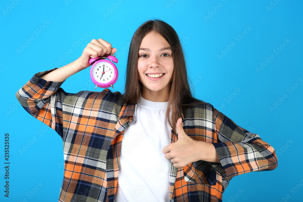 Young girl holding alarm clock on blue background Young girl holding alarm clock on blue background