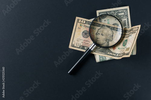 Magnifying glass and money on black background. Paper currency. Looking For Money. Concept of search. Top view. Flat lay