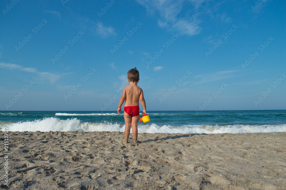 baby is dressed in swimming trunks and holds a toy watering can. baby is dressed in swimming trunks and holds a toy watering can.